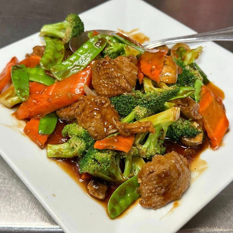 Asian Bistro's beef and broccoli stir-fry with carrots and snow peas on a white plate.