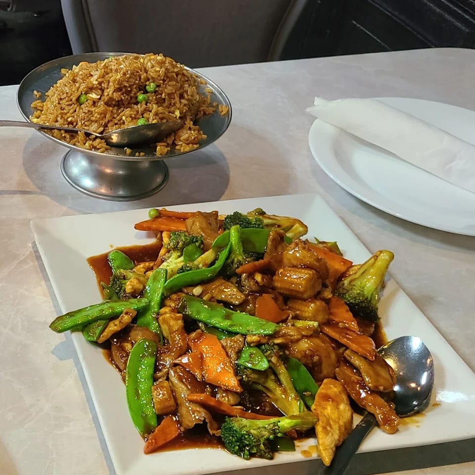 Asian Bistro's chicken and vegetable stir-fry with a side of fried rice on a white table.